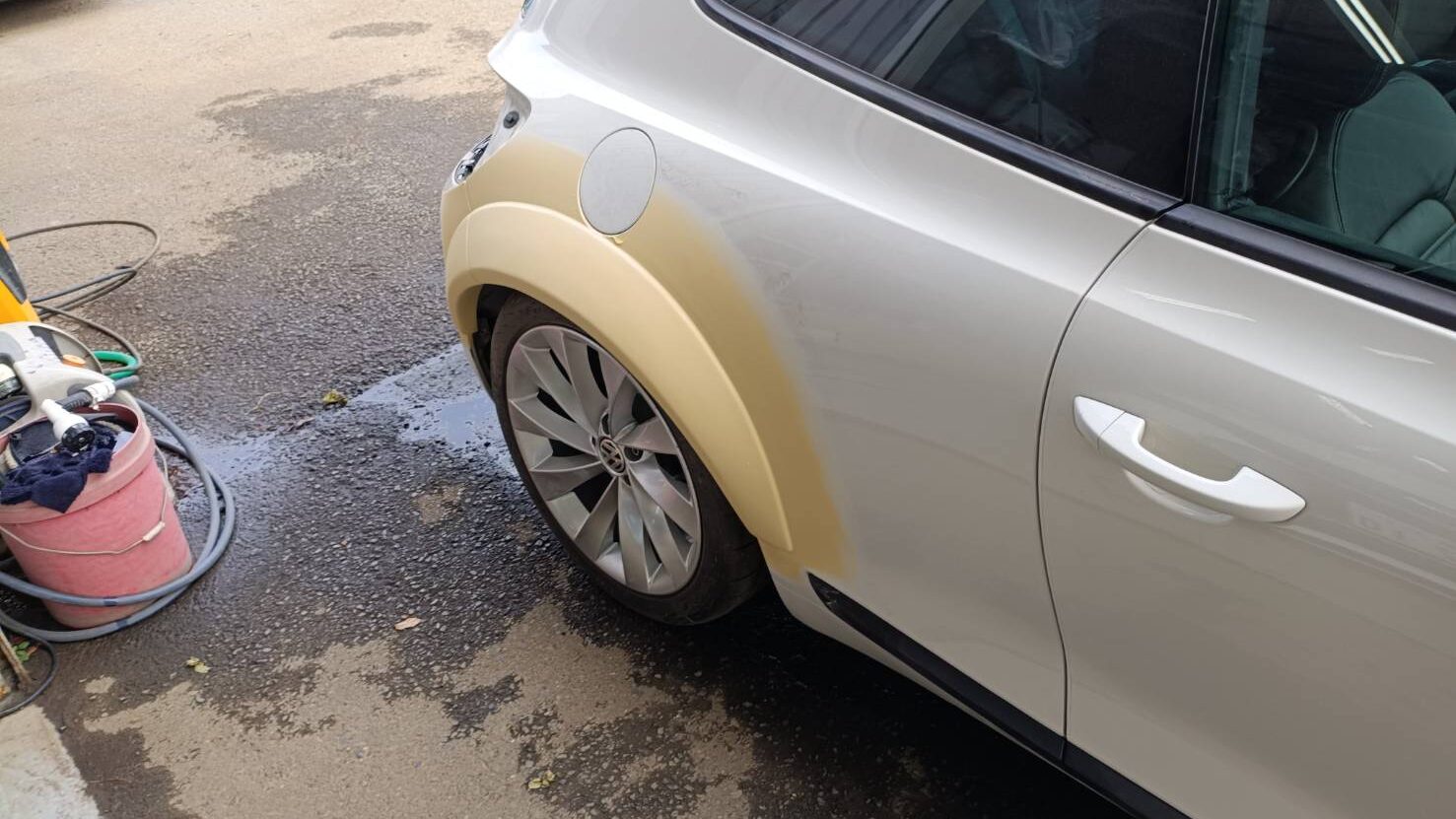 White SUV being prepped for paint with tan primer on the front fender near the wheel edge.